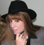Close up photo of author Mae Clair, who is wearing black fedora hat and hold pen